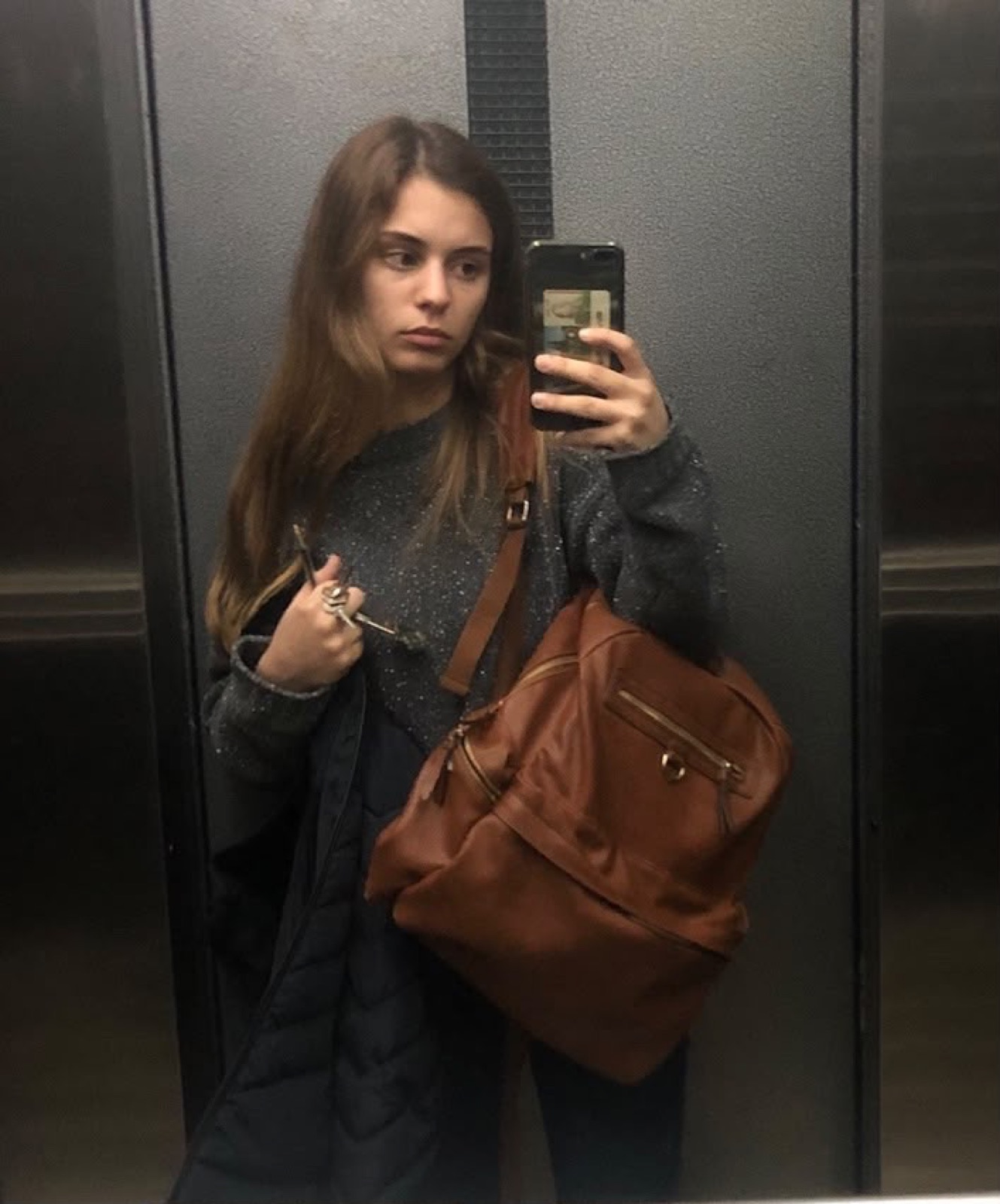 Teenage Myriam taking an elevator mirror selfie with a brown backpack